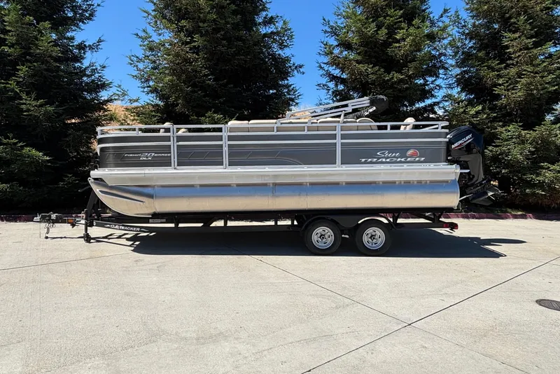 The Image of 2024 Sun Tracker Fishin' Barge 20 DLX pontoon boat on trailer, parked outdoors. - 0