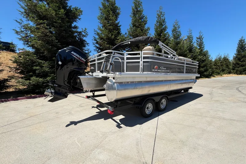 Slide: The Image of 2024 Sun Tracker Fishin' Barge 20 DLX pontoon boat on trailer, outdoor setting. - 4