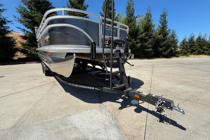 Slide: The Image of 2024 Sun Tracker Fishin' Barge 20 DLX on trailer, parked outdoors with trees in background. - 10