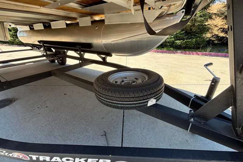Slide: The Image of 2024 Sun Tracker Fishin' Barge 20 DLX trailer with spare tire, parked outdoors. - 30