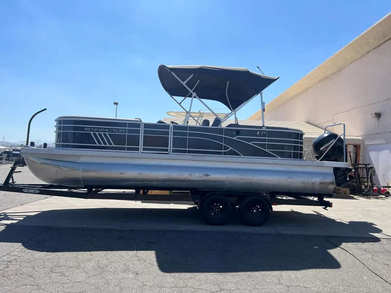 Slide: The Image of 2022 Bennington 23 L pontoon boat on a trailer in a sunny outdoor setting. - 2