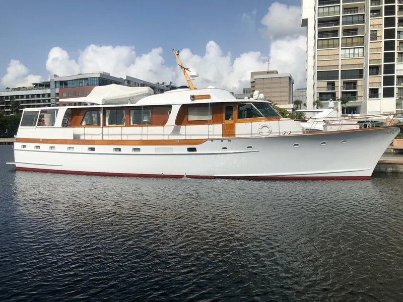 Slide: The Image of 1972 Trumpy 72 Houseboat docked in a marina with modern buildings in the background. - 1