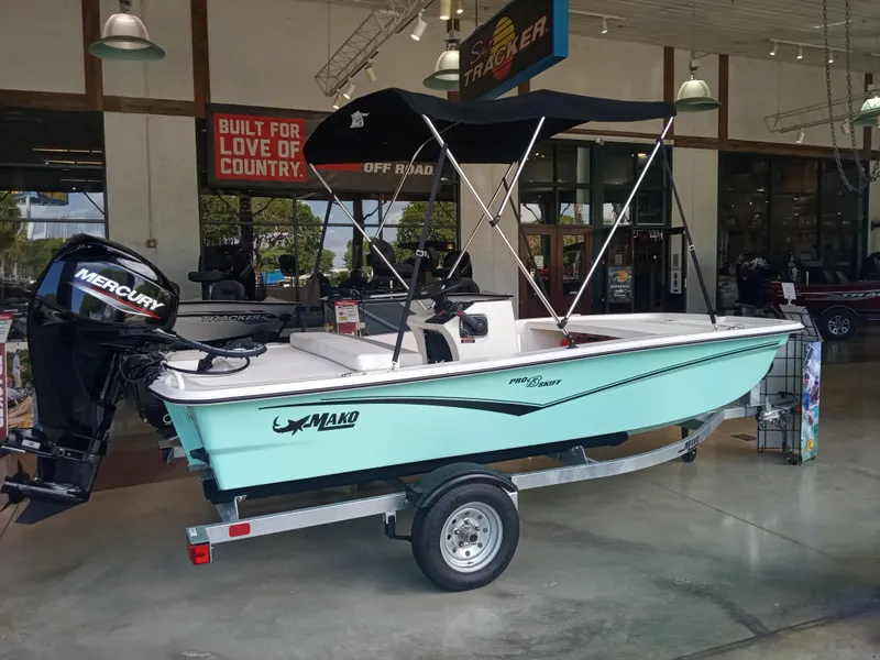 Slide: The Image of 2024 Mako Pro Skiff 13 CC boat on trailer in showroom with Mercury outboard motor. - 1