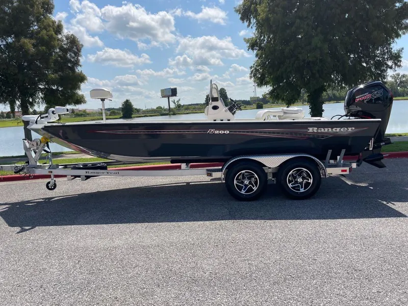 Slide: The Image of 2023 Ranger RB200 boat on a trailer by a lake under a blue sky. - 0