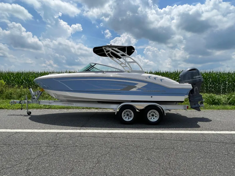 The Image of 2024 Chaparral 21 SSi OB boat on trailer, side view, with blue sky and cornfield background. - 0