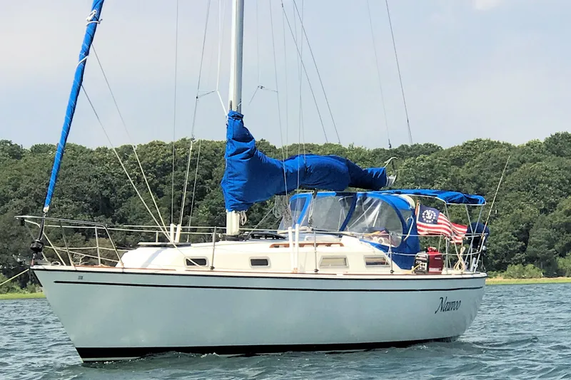 The Image of 1984 Pearson 34 sailboat with blue covers, anchored near a forested shoreline. - 0