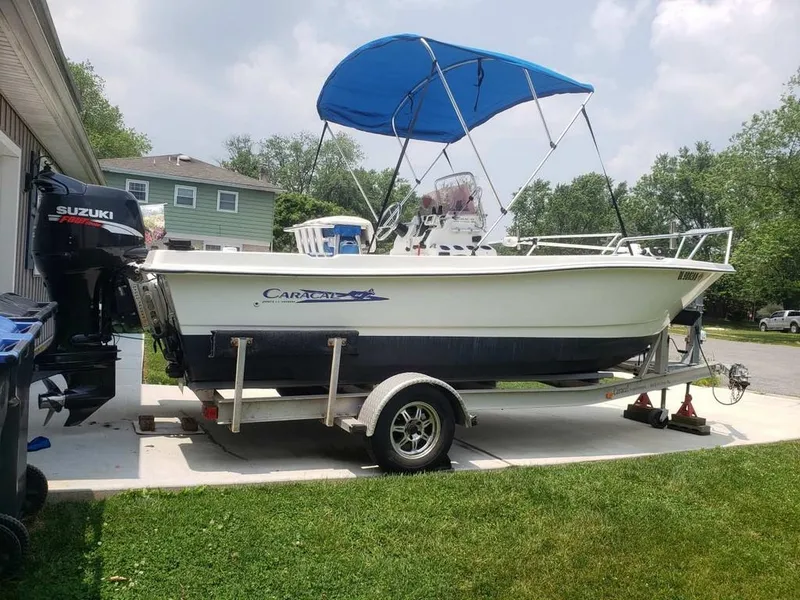 Slide: The Image of Caracal 180 boat on trailer with blue canopy, Suzuki motor, parked on driveway. - 1