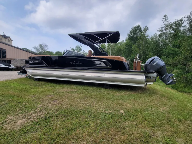 Slide: The Image of 2024 Avalon Excalibur WQL 27 Tri-Toon boat on grassy area with trees in background. - 9