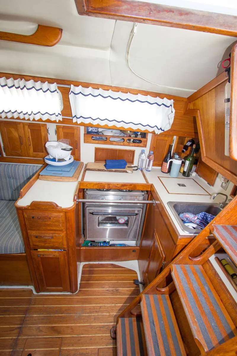 Slide: The Image of 1987 Ericson Mk III sloop interior with compact kitchen, wooden cabinetry, and nautical decor. - 6