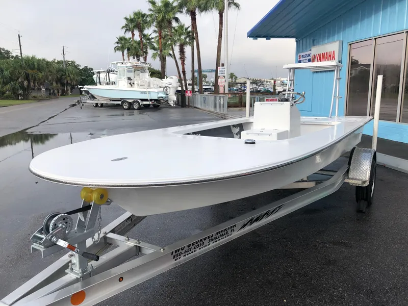 Slide: The Image of 2025 Mitzi Skiffs 17 boat on trailer, parked near a blue building with palm trees. - 7