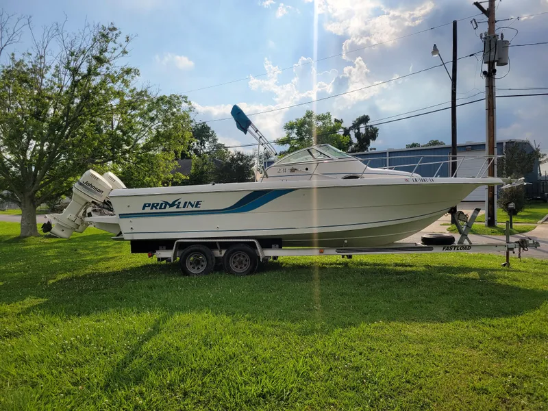 Slide: The Image of 1996 Pro-Line 231 Walk Around Cuddy boat on a trailer in a grassy area. - 2