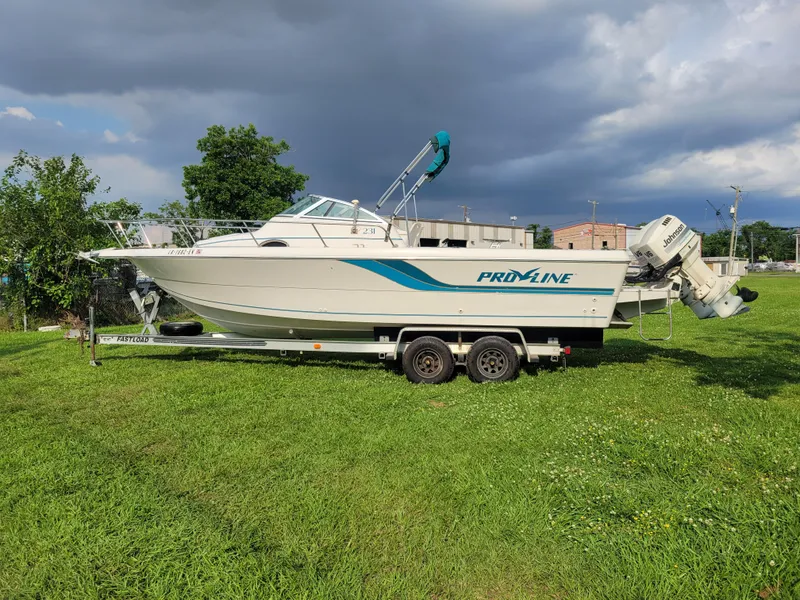 Slide: The Image of 1996 Pro-Line 231 Walk Around Cuddy boat on a trailer in a grassy area. - 6