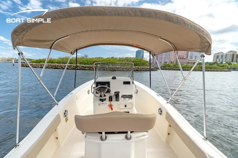 Slide: The Image of 2021 Scout 195 Sportfish boat with canopy on calm water, cityscape in background. - 6