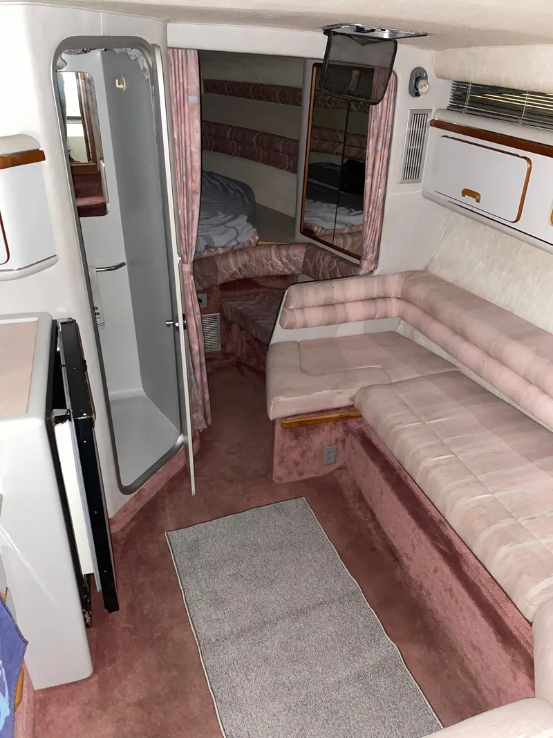 Slide: The Image of 1990 Sea Ray Sundancer interior with pink and white seating, compact kitchen, and cozy sleeping area. - 1