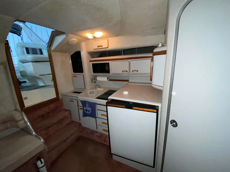 Slide: The Image of 1990 Sea Ray Sundancer interior kitchen with white cabinets and appliances. - 6