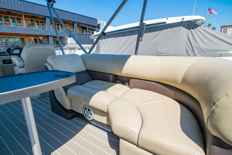 Slide: The Image of 2021 Manitou Oasis SHP pontoon boat with beige seating and table, docked near a building. - 45
