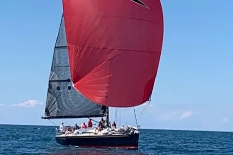 Slide: The Image of Sailboat with a red sail on open water, several people on board. - 37