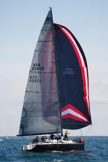 The Image of A sleek sailboat with black and red sails navigates open waters. - 1