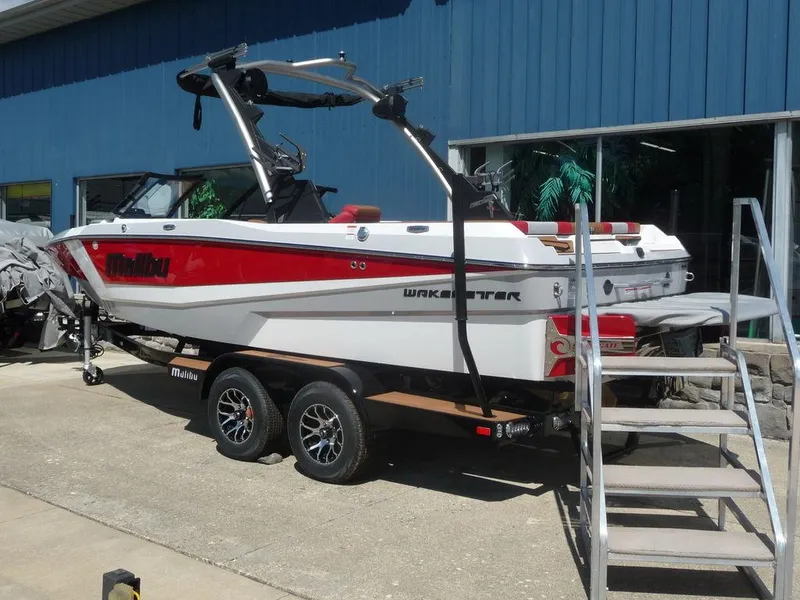 Slide: The Image of 2023 Malibu 21 LX boat on trailer outside blue building. - 19