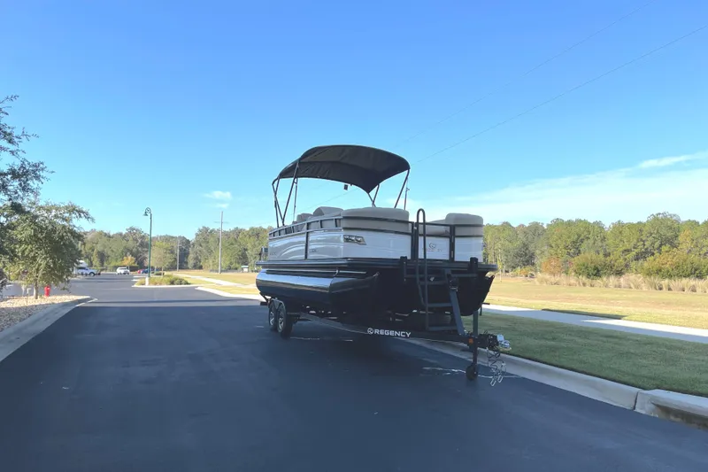 Slide: The Image of 2024 Regency 230 DL3 pontoon boat on a trailer in a suburban area. - 2