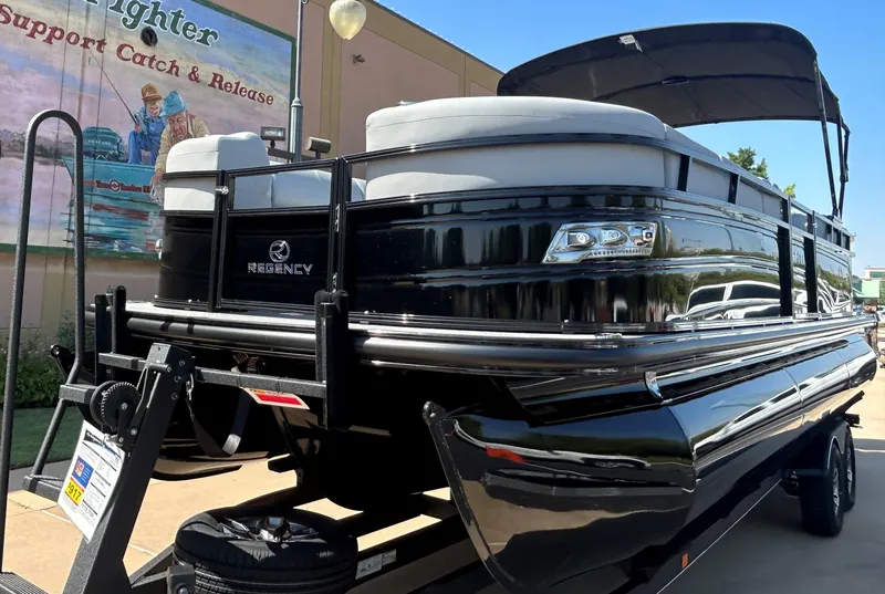 Slide: The Image of 2024 Regency 250 LE3 pontoon boat on trailer, black exterior, outdoor display. - 2