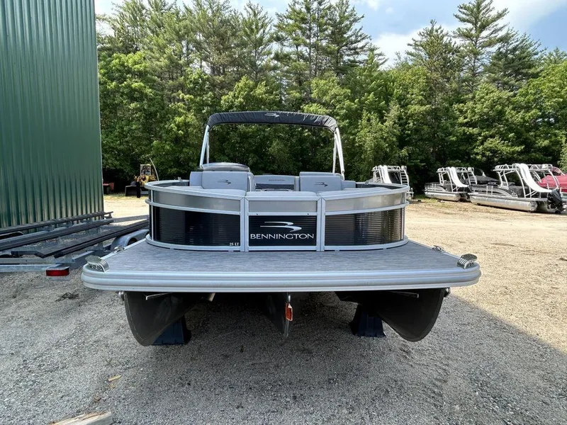 Slide: The Image of 2022 Bennington L25 pontoon boat parked on gravel lot with trees in background. - 3