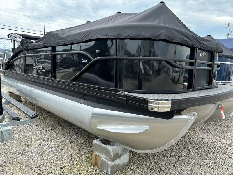 Slide: The Image of 2024 Barletta C22UC pontoon boat with black cover on gravel lot. - 1