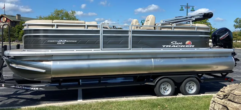Slide: The Image of 2024 Sun Tracker Party Barge 22 DLX pontoon boat on a trailer in a parking lot. - 2