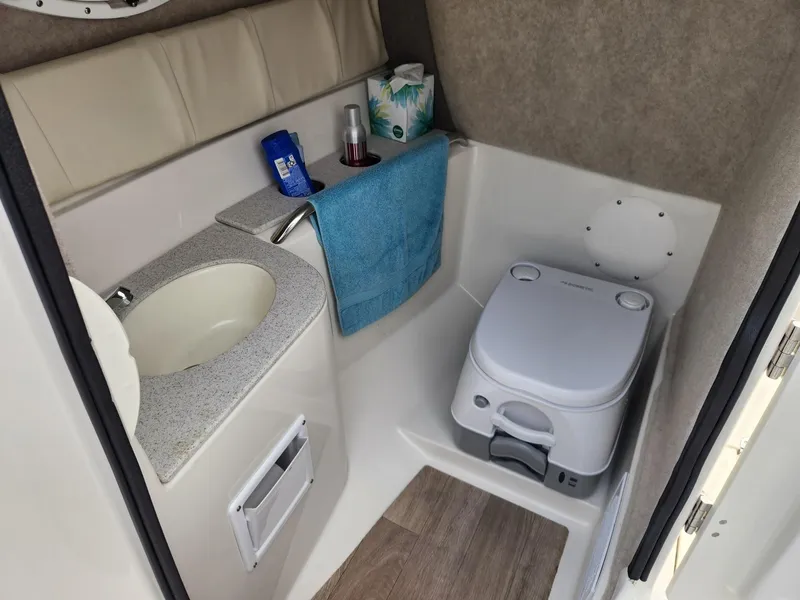 Slide: The Image of 2022 Stingray 231 DC boat bathroom with sink, portable toilet, and storage amenities. - 13