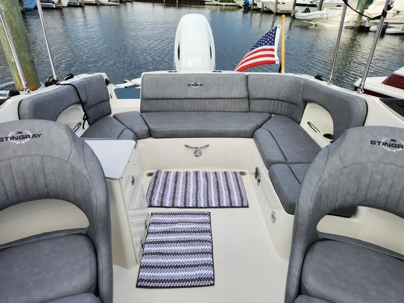 Slide: The Image of 2022 Stingray 231 DC boat interior with gray seating, American flag, and marina backdrop. - 14