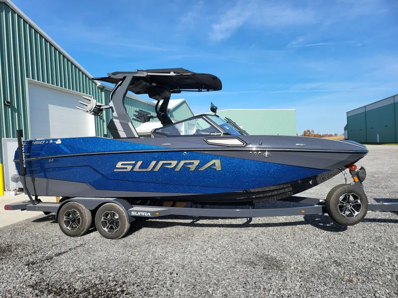 Slide: The Image of 2024 Supra SL boat on trailer, blue and black design, parked outdoors. - 0