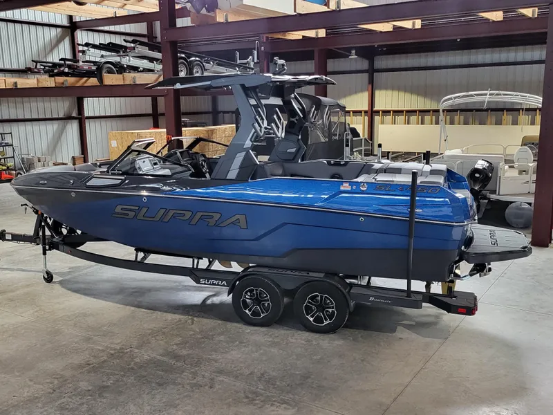 Slide: The Image of 2024 Supra SL boat in a warehouse, blue and black design on a trailer. - 18