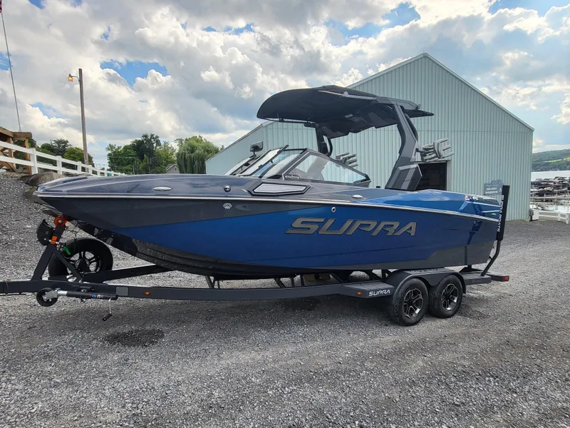 Slide: The Image of 2024 Supra SL boat on trailer, blue and black design, parked outdoors. - 24