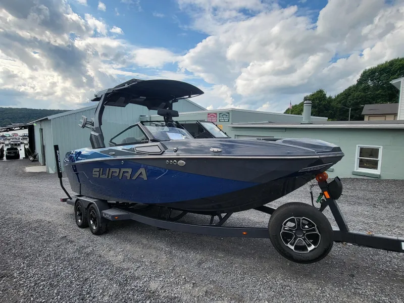 Slide: The Image of 2024 Supra SL boat on trailer, parked outdoors under cloudy sky. - 25