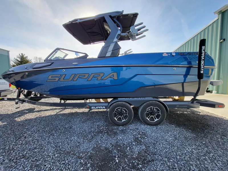 Slide: The Image of 2024 Supra SL boat in blue on a trailer, parked outdoors. - 28