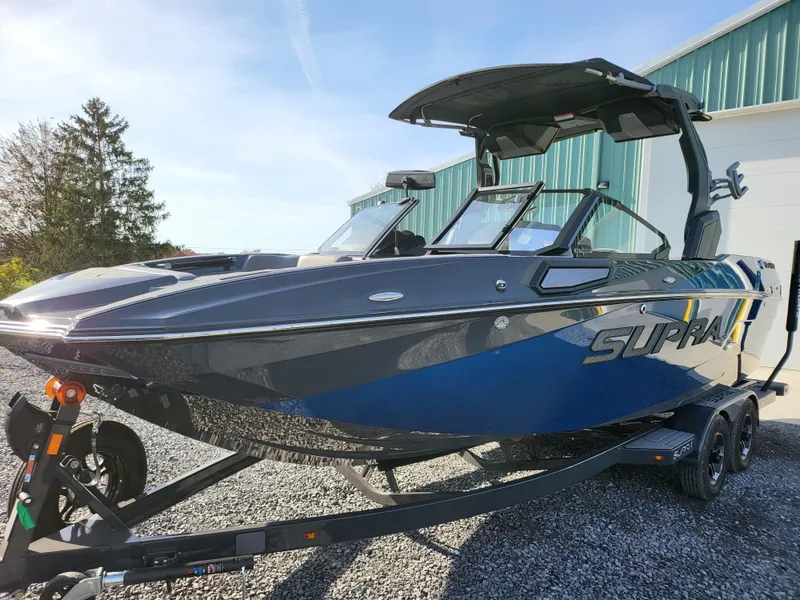 Slide: The Image of 2024 Supra SL boat on trailer, blue and gray, parked outdoors. - 30