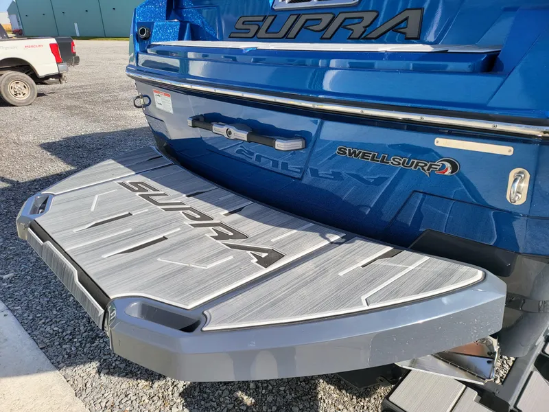 Slide: The Image of 2024 Supra SL boat with Swell Surf system, blue exterior, rear view. - 32