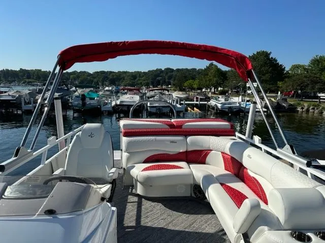 Slide: The Image of 2023 JC SportToon 24 TT pontoon boat with red and white seating at a marina. - 18