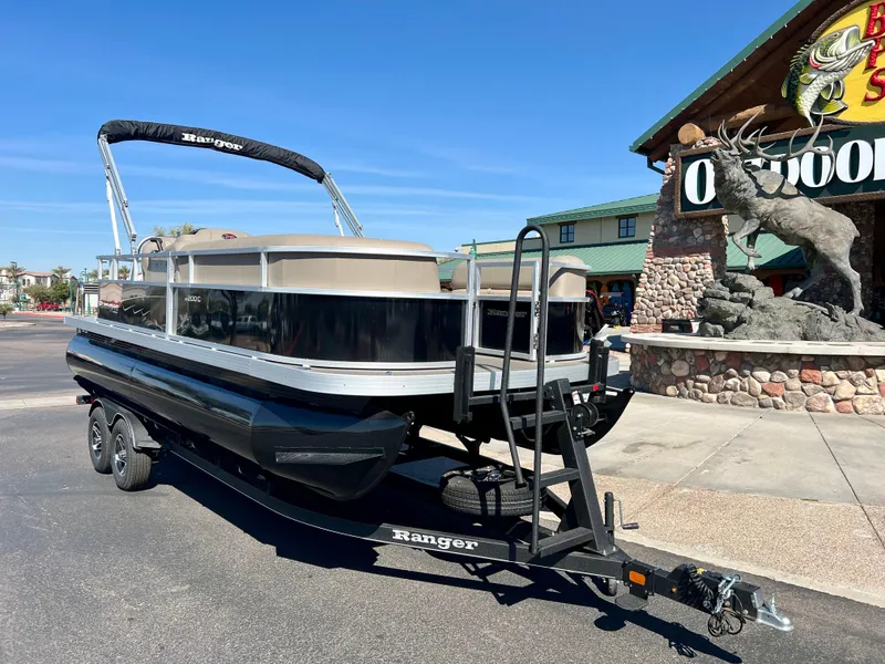 Slide: The Image of 2024 Ranger Reata 200C pontoon boat on trailer outside outdoor store. - 2