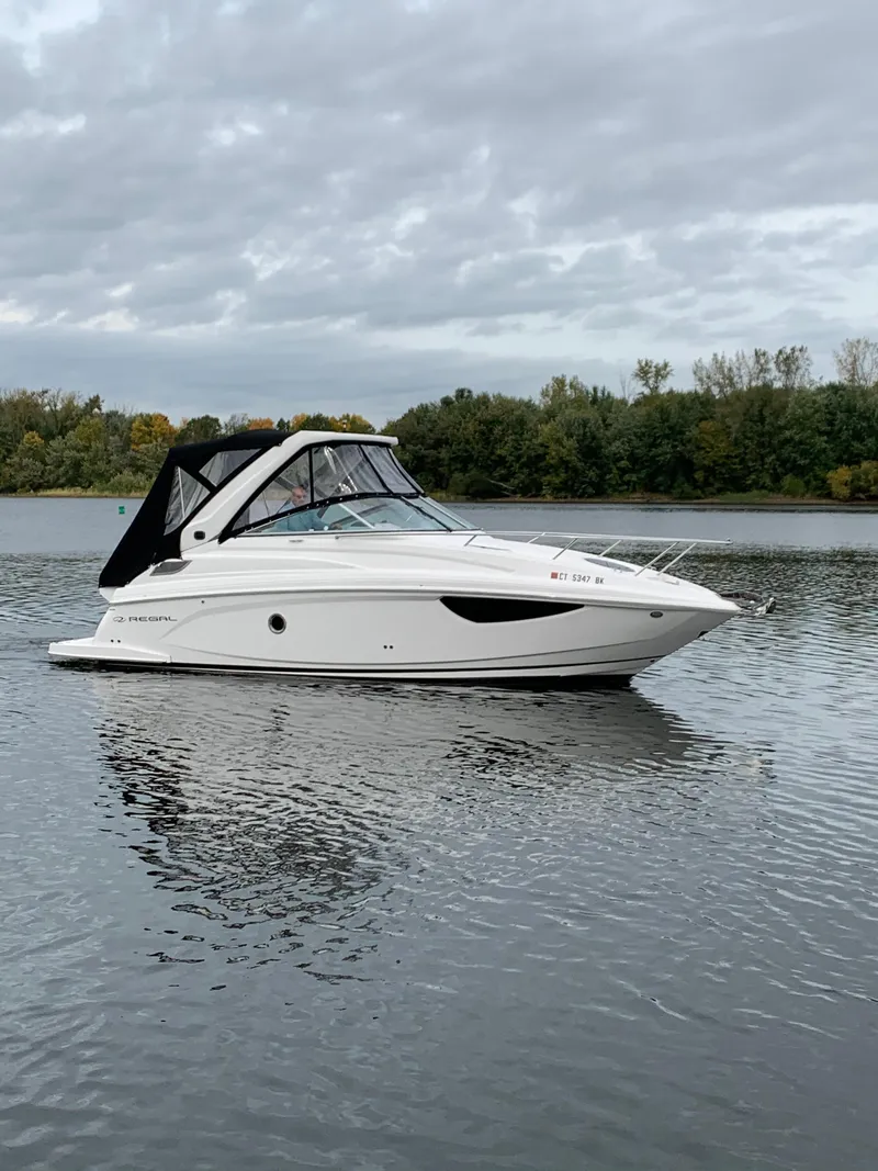 Slide: The Image of 2019 Regal 28 Express boat on a calm lake with a forested background. - 0