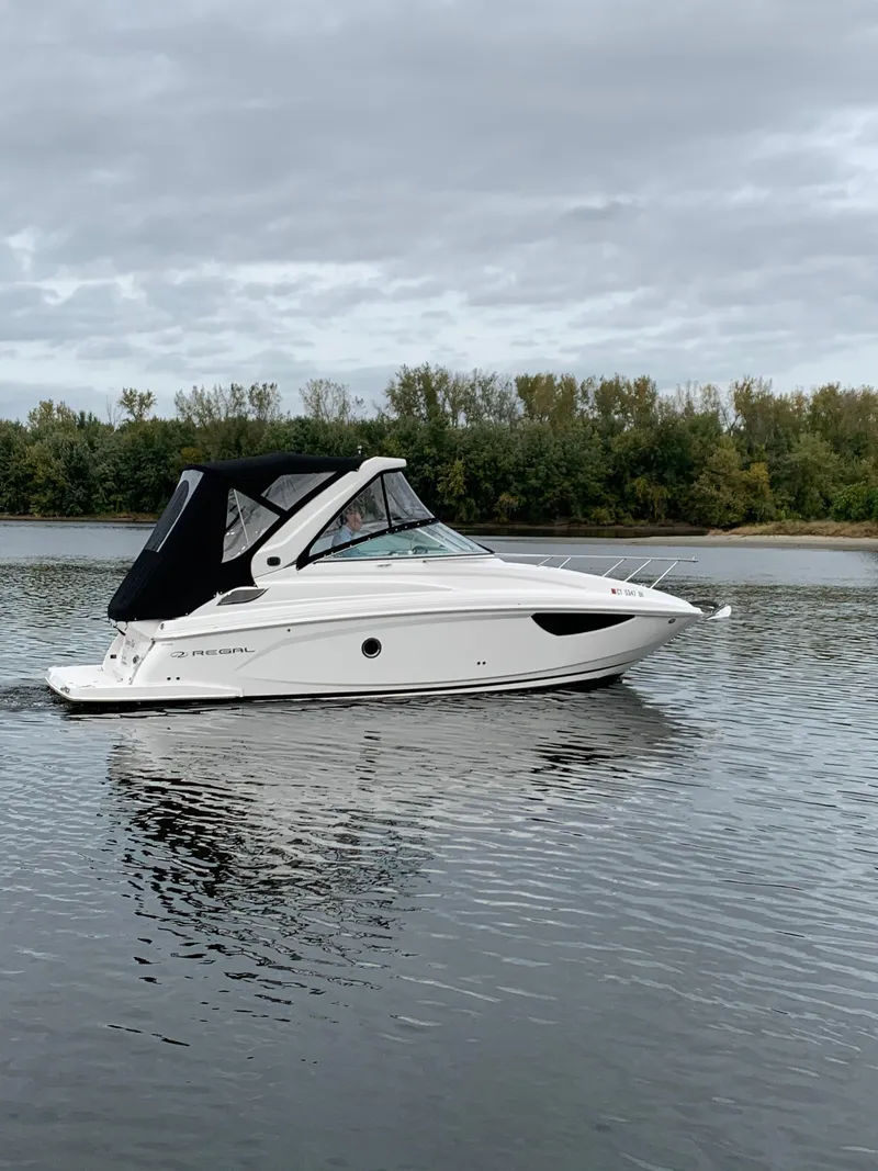 Slide: The Image of 2019 Regal 28 Express boat cruising on a calm lake with a forested shoreline. - 2