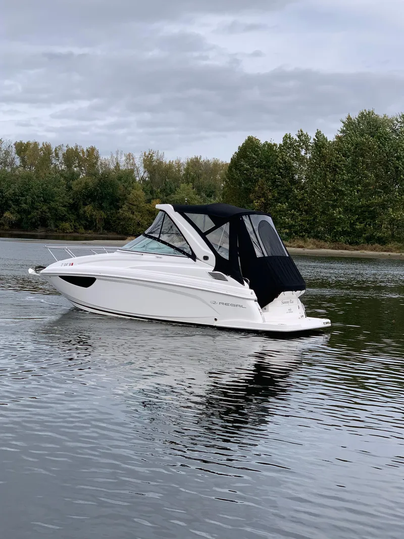 Slide: The Image of 2019 Regal 28 Express boat on a calm lake with trees in the background. - 5