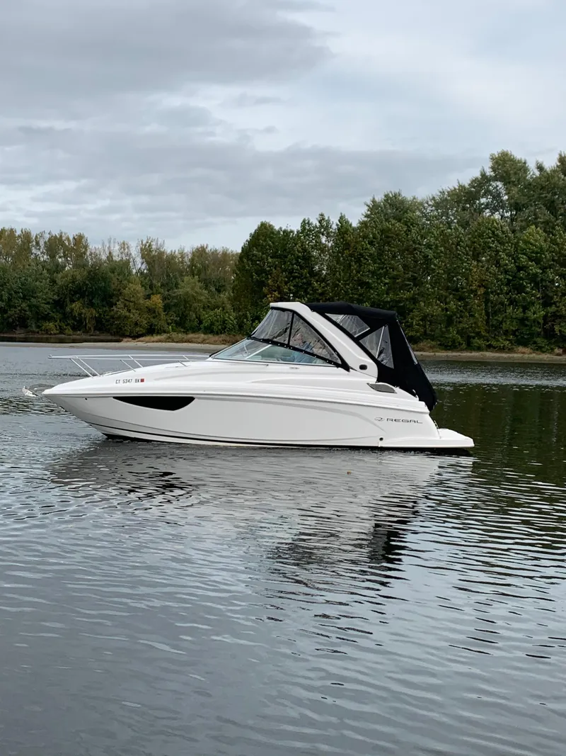 Slide: The Image of 2019 Regal 28 Express boat on a calm lake with trees in the background. - 7