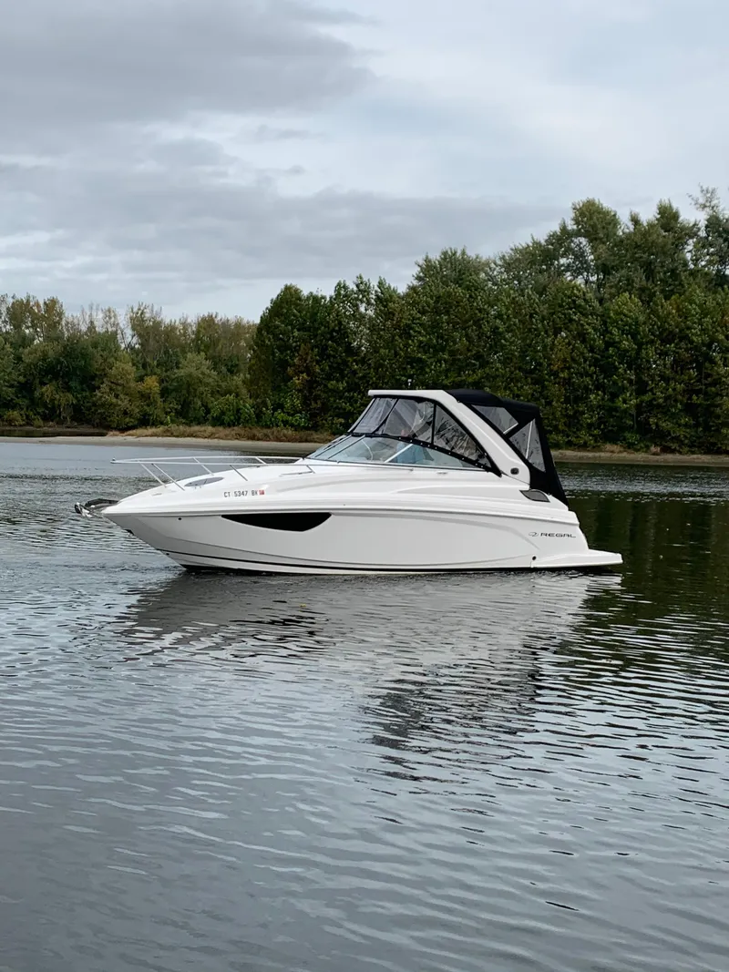 Slide: The Image of 2019 Regal 28 Express boat on a calm lake with forested background. - 8