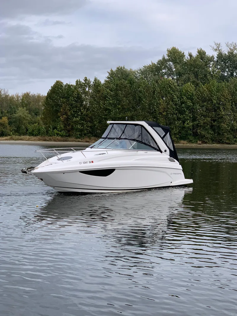 Slide: The Image of 2019 Regal 28 Express boat on a calm lake with trees in the background. - 9