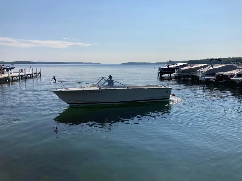Slide: The Image of 1970 Chris-Craft Lancer 23 boat cruising on a serene lake near docks. - 2