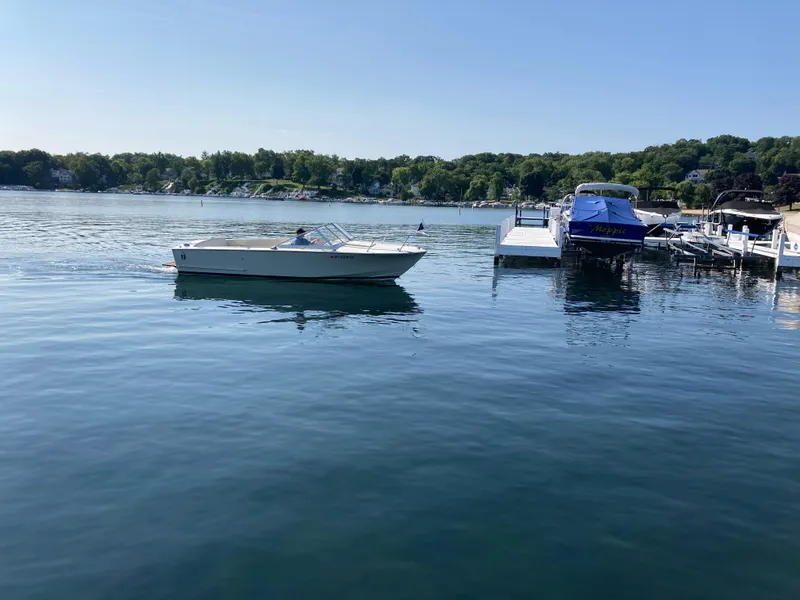 Slide: The Image of 1970 Chris-Craft Lancer 23 boat cruising on a serene lake near a dock. - 6