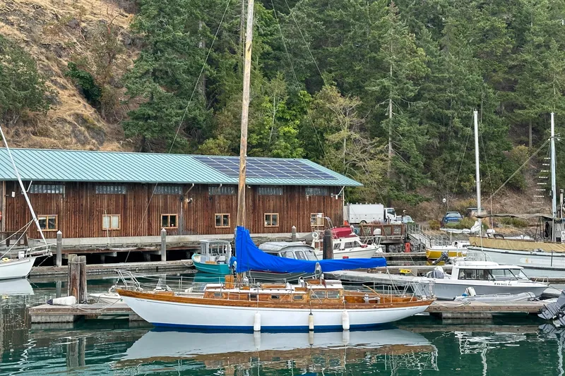 The Image of 1964 Cheoy Lee Lion Class Sloop docked at a marina with a wooden building in the background. - 0