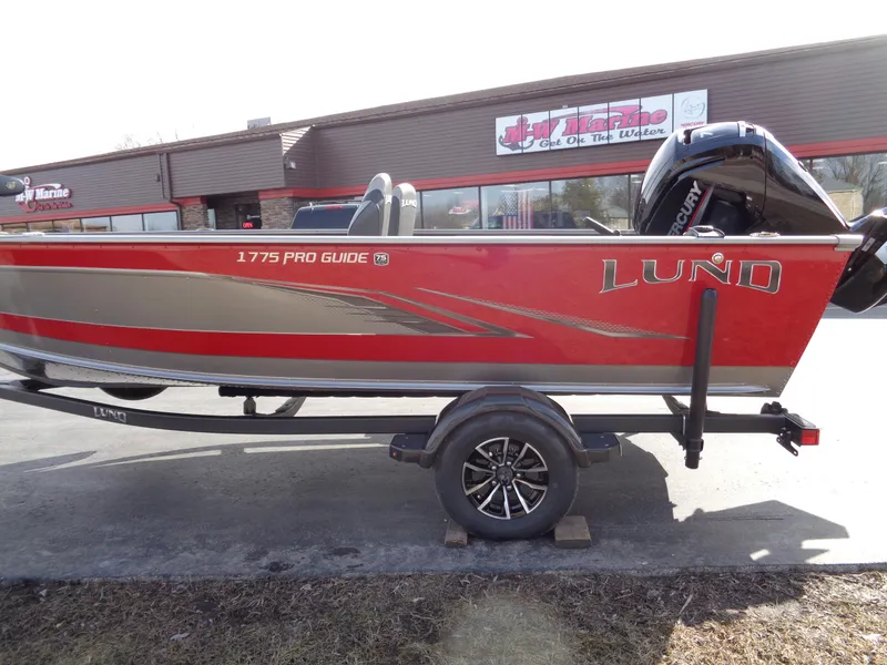 Slide: The Image of 2023 Lund 1775 Pro Guide boat on trailer, red and silver, parked outside a building. - 6