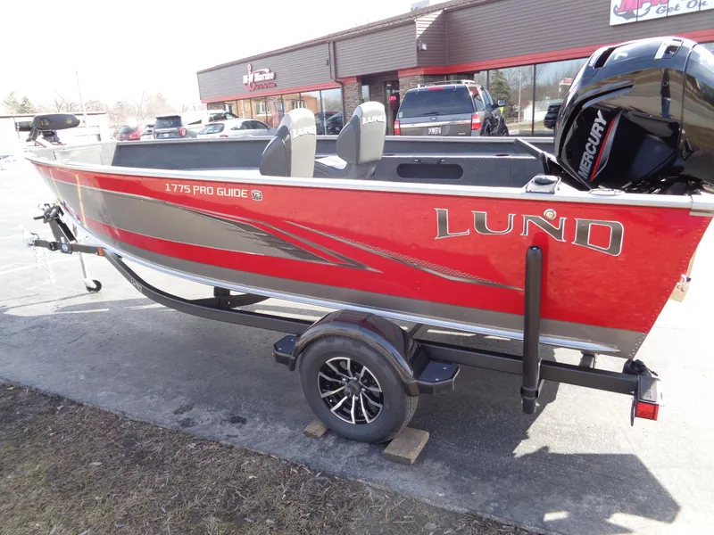 Slide: The Image of 2023 Lund 1775 Pro Guide fishing boat on trailer, red and silver, parked outside dealership. - 7